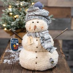 a snowman with a hat and scarf on sitting in front of a christmas tree