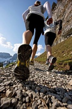 two people are running up a rocky trail together, one is holding the other's leg