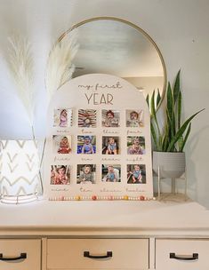 a white dresser topped with pictures and a mirror next to a potted plant on top of it