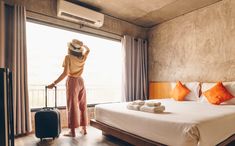 a woman standing next to a bed in a room with a suitcase and towels on it