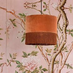 a lamp hanging from the ceiling in front of a wall with flowers and branches on it