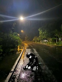 a man kneeling down on the side of a wet road at night with street lights in the background