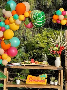 there is a table with balloons and other decorations on it in the yard, along with some plants