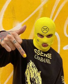 a person wearing a yellow mask pointing at the camera with their finger in front of them