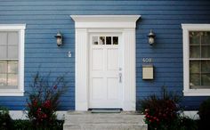 a blue house with white trim and two windows on the front door is seen in this image