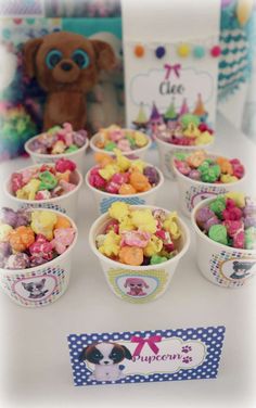 a table topped with lots of cupcakes and small bowls filled with candy next to a teddy bear