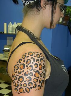 a woman with a leopard print tattoo on her arm and shoulder is looking down at the floor