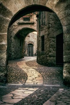 an alley way with cobblestones and arched doorway leading to another building in the distance