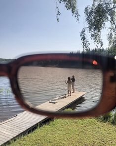 two people standing on a dock in front of a pair of glasses that are reflecting them