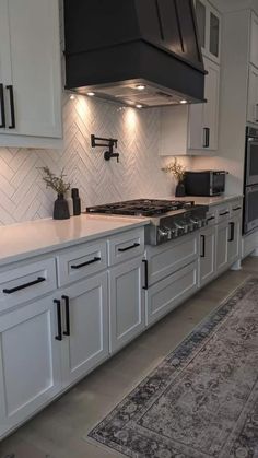 a kitchen with white cabinets and black stove top hood over the range in front of an area rug