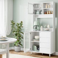 a kitchen with green walls and white furniture in the center, including an open shelving unit next to a potted plant