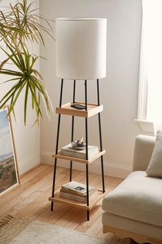 a white lamp sitting on top of a wooden shelf next to a couch and a potted plant