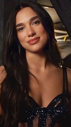 a woman with long dark hair wearing a black dress and posing for the camera in front of a car