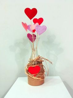 a vase filled with paper hearts sitting on top of a white table next to a plant