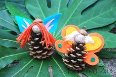 two pine cones are sitting on top of some green leaves and one is made to look like a fairy