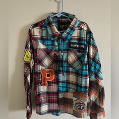 a plaid shirt with patches hanging from a hook on a wall next to a coat rack