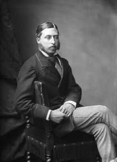 black and white photograph of a man in suit sitting on a chair with his legs crossed