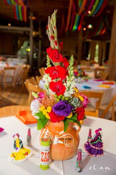 an orange vase filled with colorful flowers on top of a white tablecloth covered table