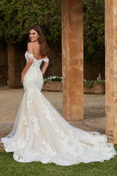 a woman in a white wedding dress standing on the grass with her back to the camera