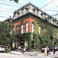 people crossing the street in front of an old brick building with ivy growing on it