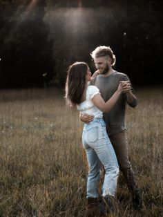 a man and woman standing in the middle of a field with their arms around each other