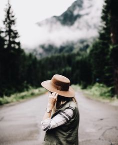 a woman wearing a hat is talking on her cell phone while walking down the road