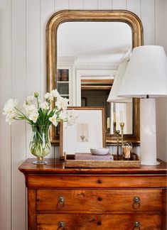 an image of a dresser with flowers on it and a mirror in the corner behind it