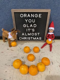 an elf is standing next to oranges and a sign that says orange you glad it's almost christmas