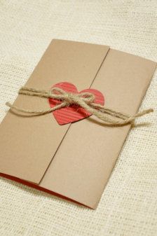 a brown envelope with a red heart on it tied up to a string and sitting on top of a white cloth