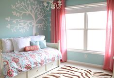 a bedroom decorated in blue and pink with a tree painted on the wall