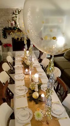 a table set for a birthday party with balloons and candles in the center, surrounded by white chairs