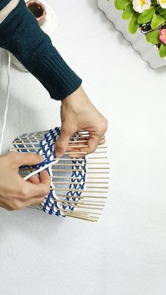 a person holding a bamboo comb over a blue and white basket with flowers in the background