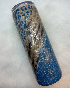 a blue and silver tumbler sitting on top of a white fur covered floor with gold flakes