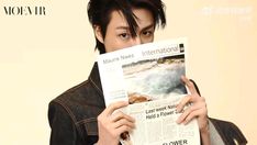 a young man holding up a newspaper with the cover pulled over his face and looking at the camera