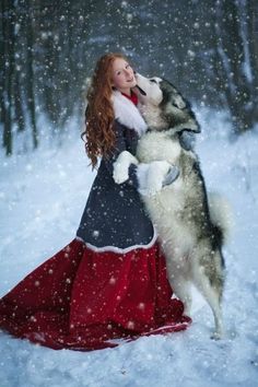 a woman in a red dress is hugging a husky dog on the snow covered ground