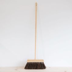 a broom sitting on top of a wooden table next to a white wall and floor