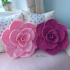 three pink and purple flower pillows sitting on a couch next to a window with curtains