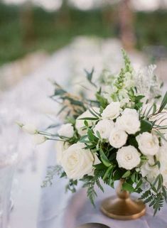 a vase with white flowers and greenery sits on a silver table cloth at an outdoor wedding reception