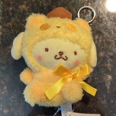 a yellow stuffed animal keychain with a gold bow around it's neck