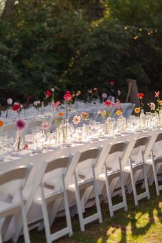 a long table is set with white chairs and flowers in vases on the tables