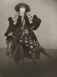 an old fashion photo of a woman in a dress and fur coat sitting on a chair