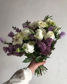 a hand holding a bouquet of white and purple flowers