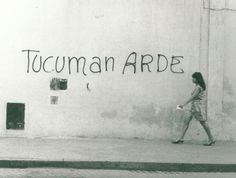 a woman walking down the street in front of a wall that has writing on it