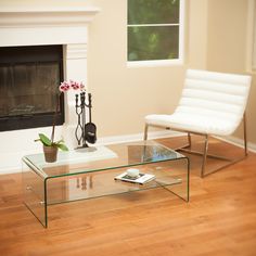 a living room with a glass coffee table and white chair in front of a fireplace