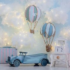 two hot air balloons and a toy car in front of a wall with clouds on it