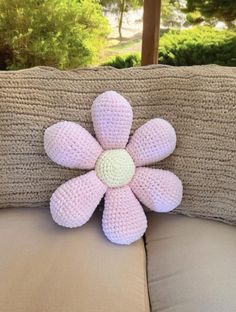 a pink crocheted flower sitting on top of a couch next to a window