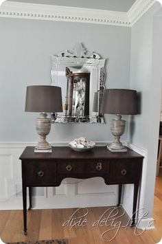 a table with two lamps and a mirror on top of it next to a wall