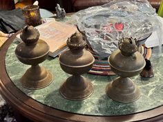 three bronze candlesticks sitting on top of a glass table with books and other items