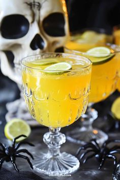 two glasses filled with yellow liquid and topped with limes next to a white skull