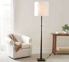 a living room with a white chair and a lamp on the floor next to a table